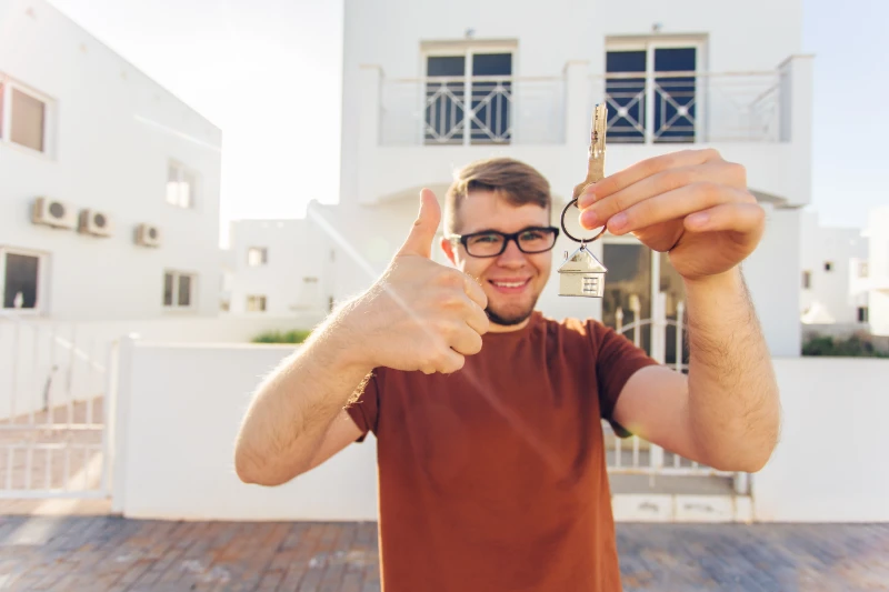 Young man with keys in from of his home.